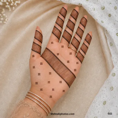 Front hand with fine striped mehndi enclosed in bold diagonal bands across the fingers and palm, finished with small dot clusters.