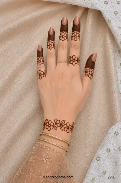 Back hand with dark filled fingertips, simple floral finger motifs and a delicate flower-and-leaf mehndi band around the wrist.