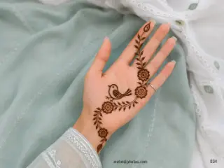 Front hand mehndi design featuring a small bird surrounded by rounded flowers and a flowing leafy vine from the wrist to one finger