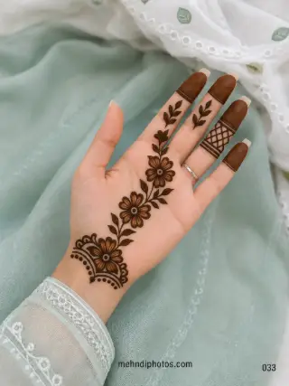 Front hand mehndi design with a diagonal Arabic floral vine, shaded flowers, dark leaves, filled fingertips and a lattice finger accent