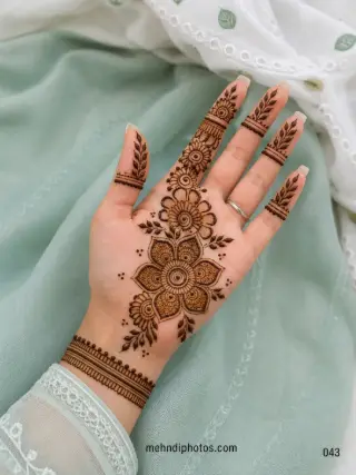 Front hand mehndi design featuring a large layered flower, smaller blossoms, leafy branches, finger motifs and a bracelet-style wrist band